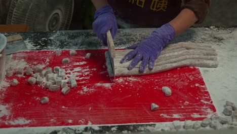 Dust-some-flour-onto-rolled-cylindrical-shapes-of-taro-dough,-chop-them-into-small-portions-using-a-dough-cutter,-close-up-shot-preparation-of-yam-balls,-the-popular-traditional-Taiwanese-dessert