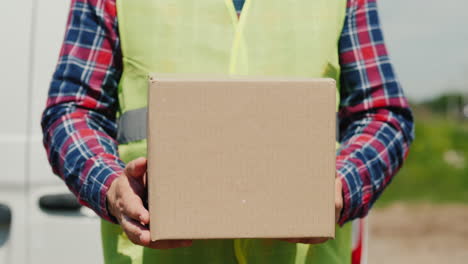 a courier with a cardboard box stands against the background of a white delivery service van