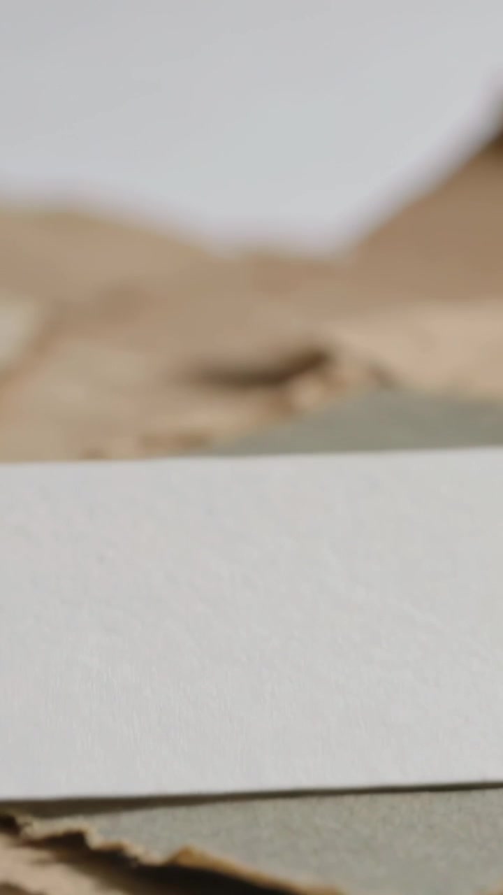 Vertical video: Panning cam back revealing center paper pile on desk with white card grey mat kraft