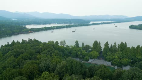 overcast drone view of hangzhou’s west lake with boats, green canopy below