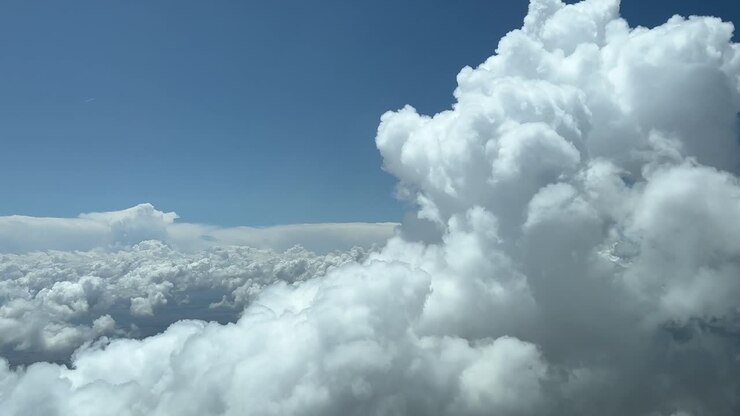 A pilot’s point of view from an airplane cabin while flying through a tiny white cumulus in a sunny day with a deep blue sky