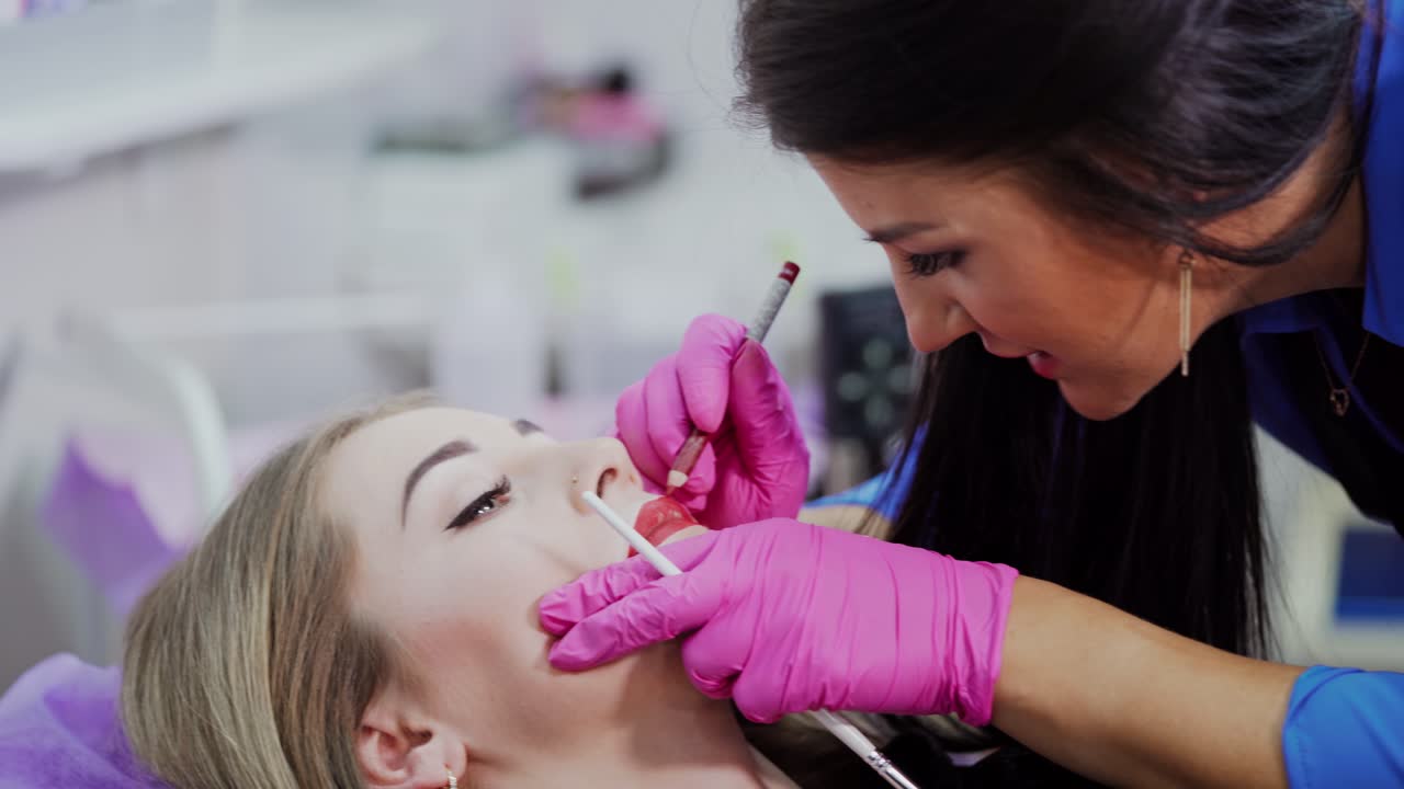 Cosmetic procedure of tattoo on lips. Master applying red permanent makeup on young girl lips. Close-up. Plastic medicine and cosmetology.
