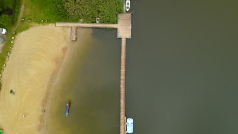 ascend top down of sandy beach and wooden jetty during sunny day at hartowiec lake in poland