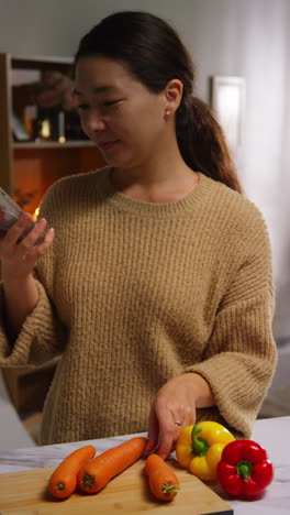 vertical video of woman talking on mobile phone at home preparing fresh vegetables for meal on counter in kitchen 3