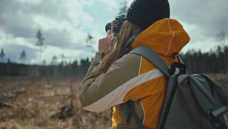 blonde woman taking pictures with digital camera while hiking in nature