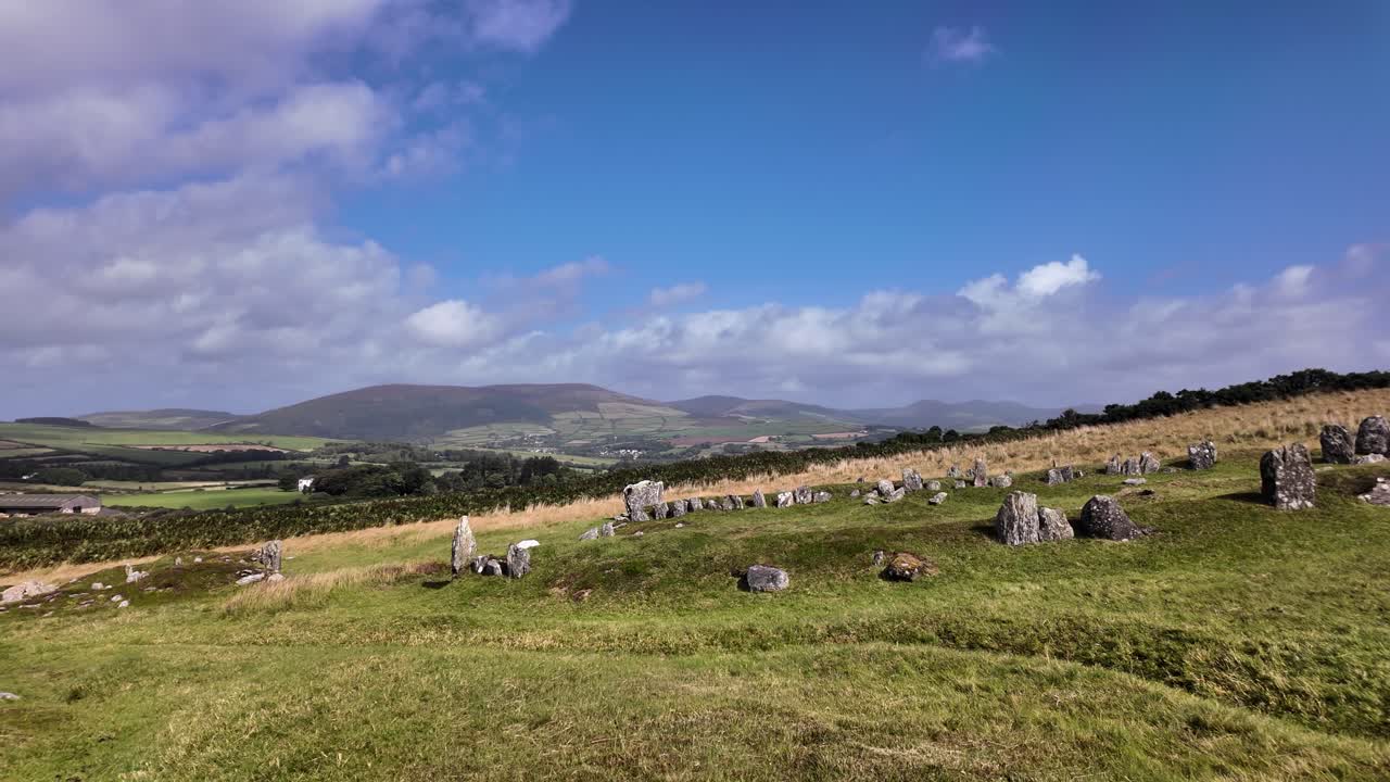 Iron Age roundhouse remains visible on a grassy hillside under a blue sky. slow pan left