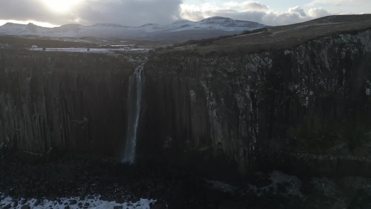 majestuosa cascada de kilt rock en skye, escocia, con montañas cubiertas de nieve en el fondo al anochecer
