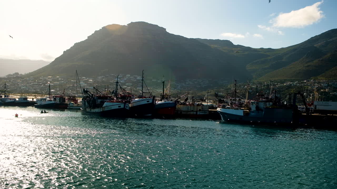 Barca rientra nel porto di Hout Bay, sole del mattino con kayakisti