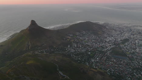 Aerial-panoramic-footage-of-city-on-ocean-coast-at-twilight.-Pink-sky-above-horizon.-Cape-Town,-South-Africa