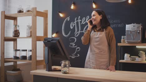 Female-Waitress-Talking-On-The-Phone-Behind-The-Counter-In-A-Coffee-Shop