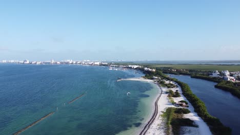 Aerial-Drone-View-of-the-Cancun-Coastline,-with-hotels-in-the-distance-and-a-kite-surfer-over-clear-blue-ocean-waters