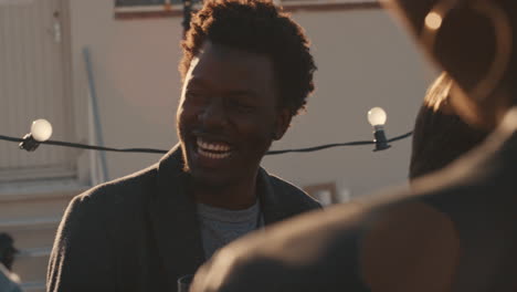 group-of-diverse-friends-hanging-out-together-enjoying-rooftop-party-at-sunset-happy-african-american-man-socializing-drinking-alcohol-having-fun-on-weekend-celebration