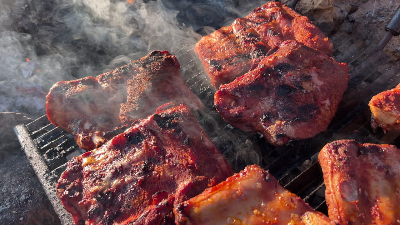 cocinar jugosas costillas de cerdo a la parrilla en una parrilla de fuego al aire libre con humo y cenizas, comida deliciosa, tiro estático de 4k