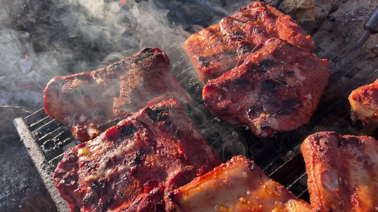 Memasak iga babi BBQ yang lezat di atas panggangan api luar ruangan dengan asap dan abu, makanan nikmat, rekaman statis 4K