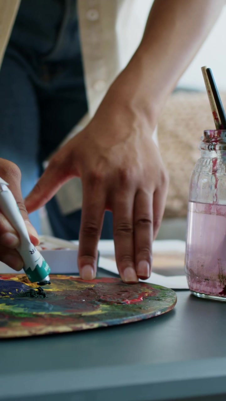 Vertical video: Painter pressing green tube squeezing on palette placing in tray preparing to paint