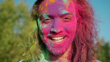 close-up slow motion portrait of carefree arab man smiling looking at camera with face covered with gulal paint