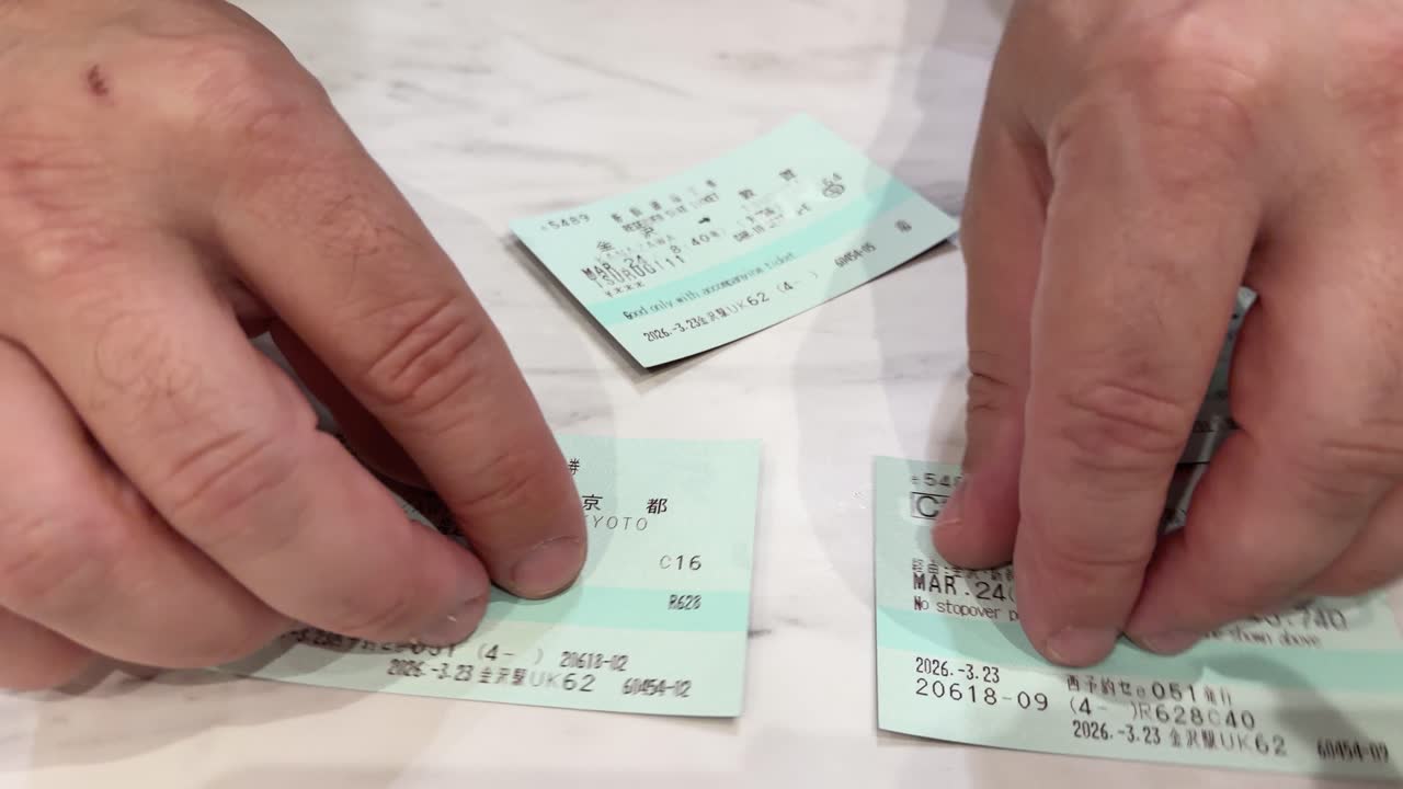 Close-up shot of hands organizing green Japanese train tickets on a white marble surface