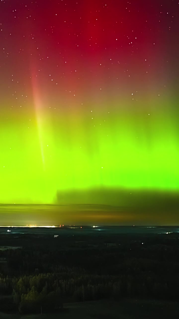 Luci verdi e rosse dell'aurora boreale danzano su un paesaggio rurale scuro di notte.