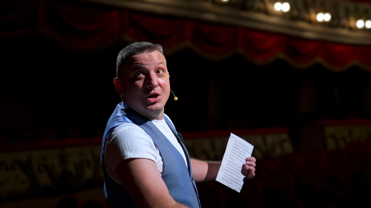 Man entertainer, presenter or actor on stage. Active gestures of throwing to the auditorium. View of a male public speaker speaking at the microphone, pointing in front.