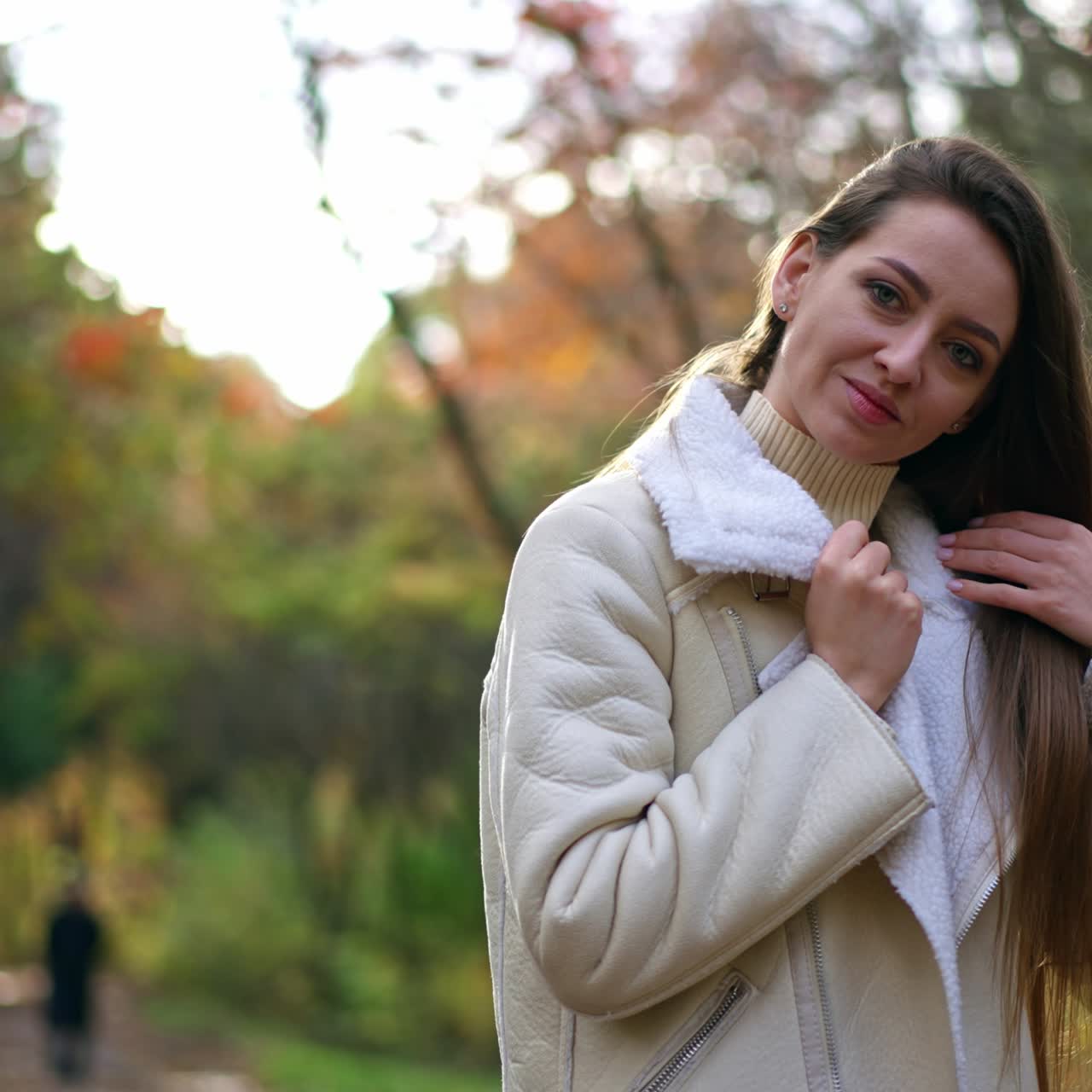 Beautiful Caucasian lady in white jacket turning in front of camera and waving her long hair. A walk by the autumn park on sunny day