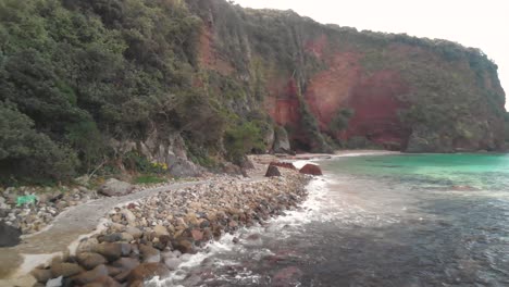 fpv aerial flight alongside stunning red cliffs and stone path next to beautiful turquoise ocean water