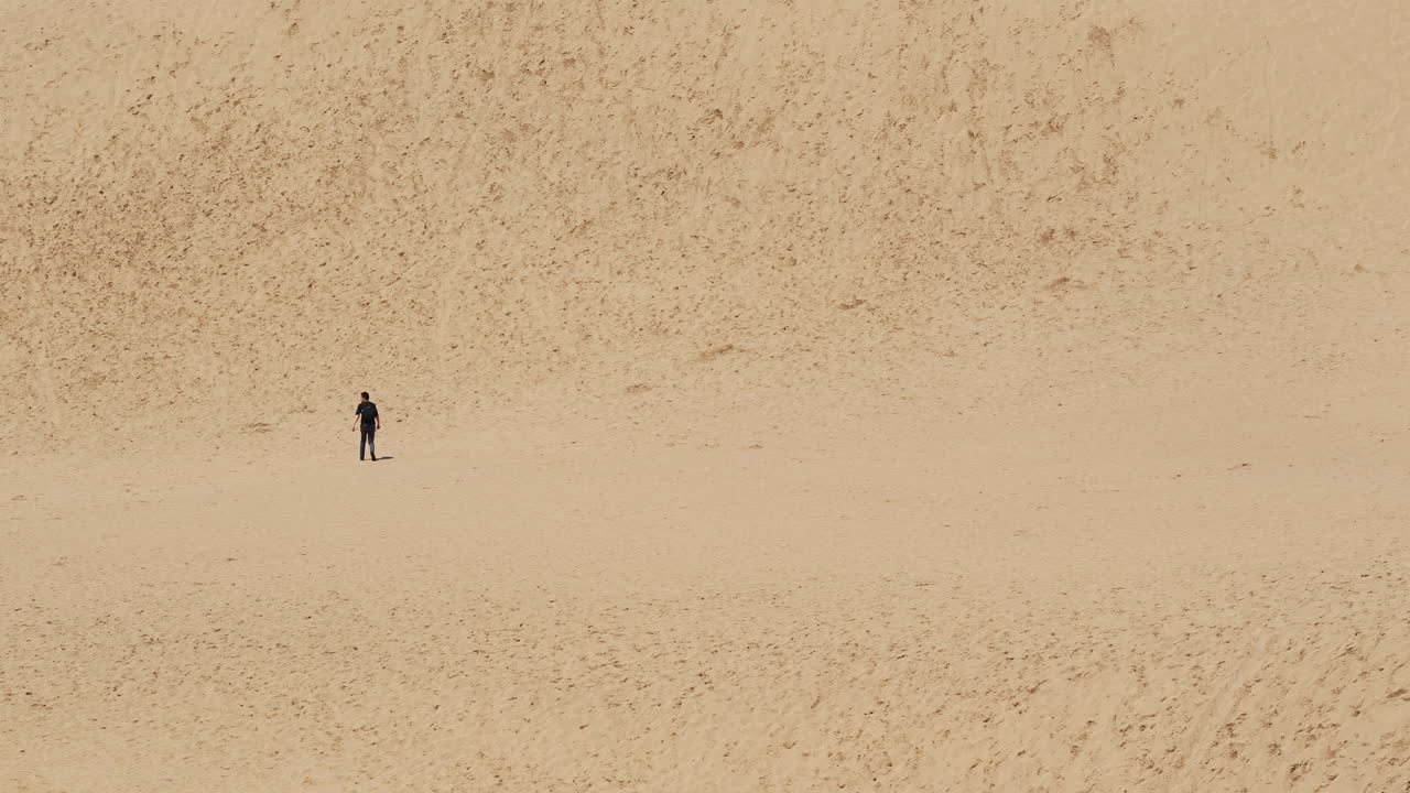 Lone traveler traversing serene sand hills against clear horizon
