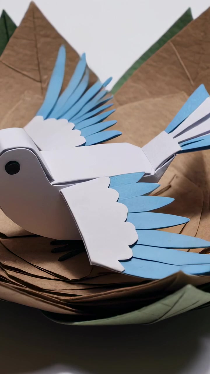 Vertical video: Flapping paper bird causing paper flower petals to fold on white table, protecting