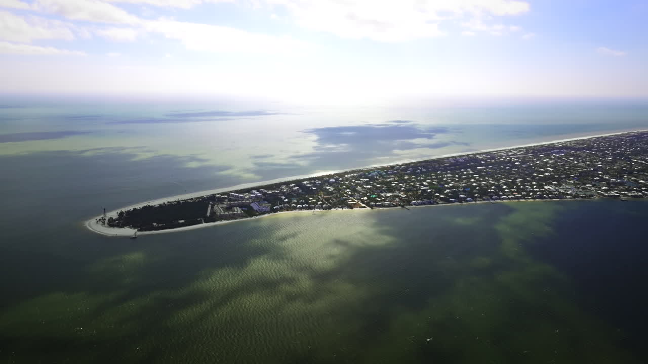 Elokuvamainen, korkealla lentävä laajakulmainen dronen ilmakuva, joka kiertää historiallisen Sanibel Islandin majakan lahden puolella ja Sanibel Islandin itäkärjen, Floridassa, kirkkaan rannikon kanssa.
