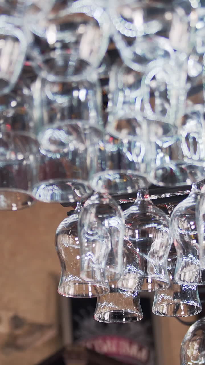 Clean washed and polished glasses for wine hanging over a bar rack. Empty wine glasses in the restaurant. Vertical video.