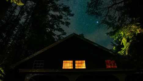 timelapse of stars behind a rustic cozy cabin in the woods of new england on a summer evening with the milky way visible behind thin clouds passing by