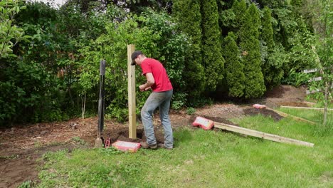 Man-setting-down-fence-pole-with-level-tool-and-pouring-cement-after