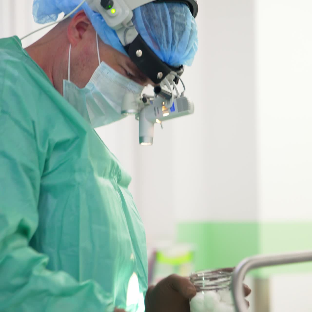 Specialist in surgery preparing the patient for the operation. Doctor in device glasses, cap and mask takes forceps and sponge to clean the patient's face