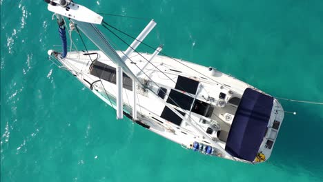 Birdseye-Aerial-View-of-Sailboat-Anchored-in-Turquoise-Tropical-Sea,-Top-Down-Drone-Shot-of-Mast-and-Deck