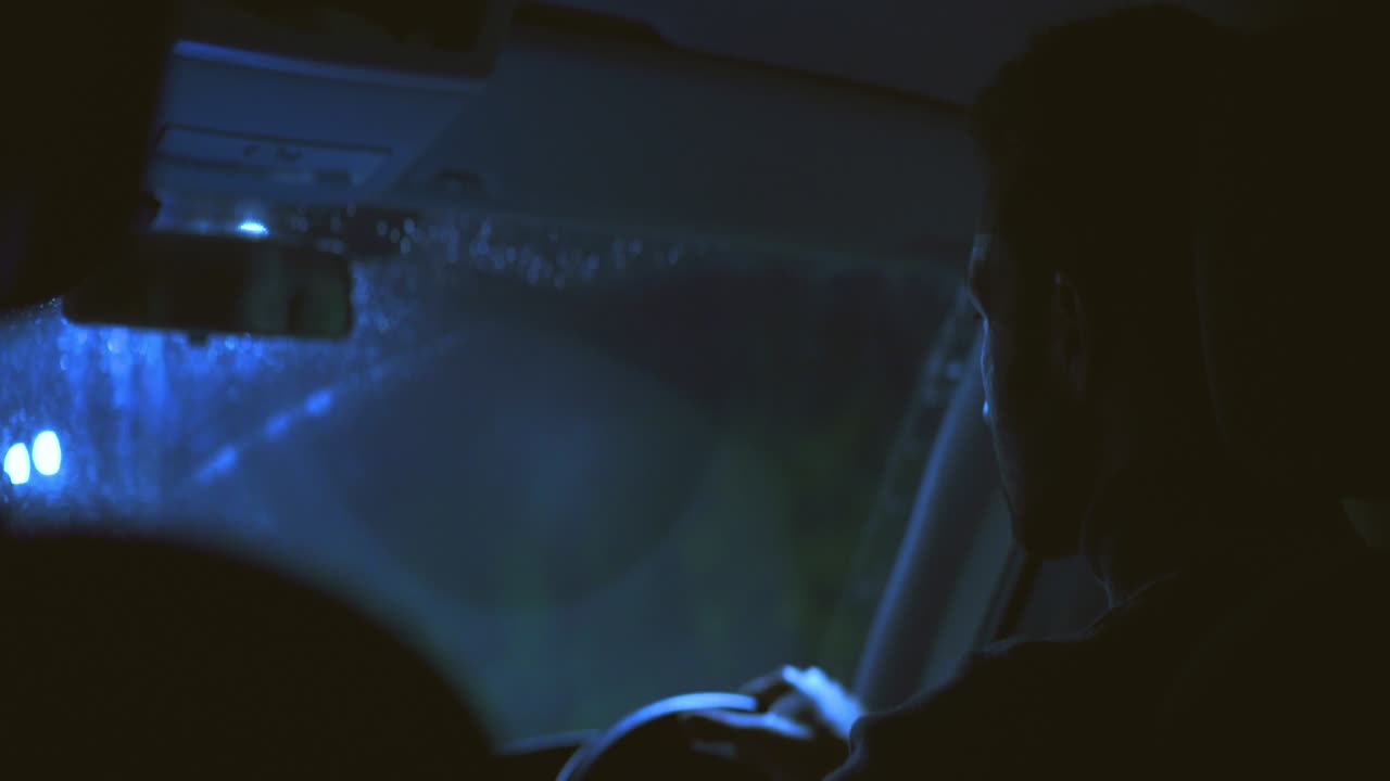 The handsome man drives the car through the night rainy road
