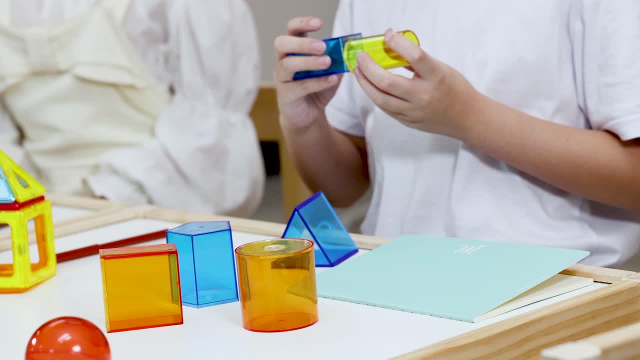 Student explores translucent geometric solids on desk under bright indoor lighting, static camera angle