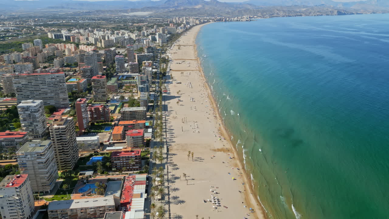 Aerial drone view of the buildings along the coastline with people relaxing on the beach in Benidorm, Spain in daylight