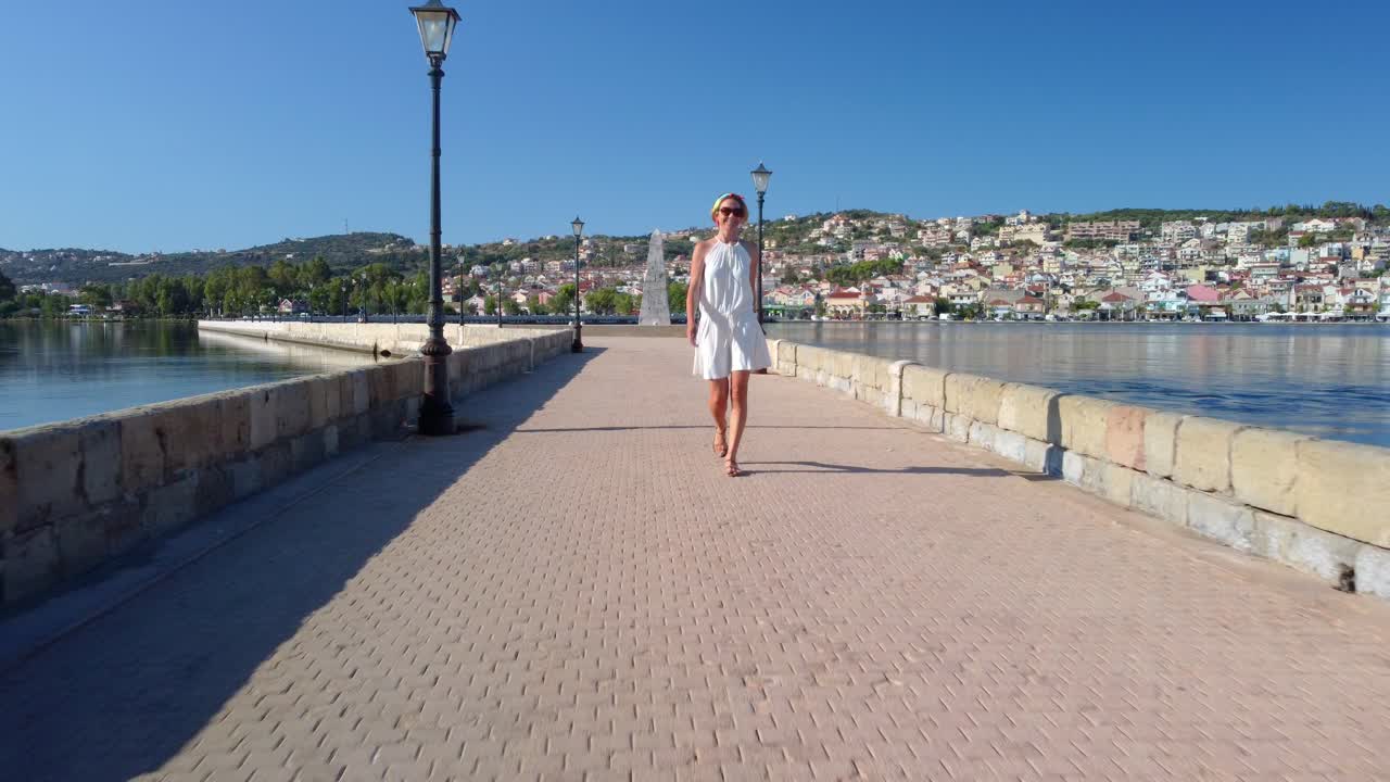 Turismo in Grecia. Vista frontale di una donna in abito bianco che cammina sul Ponte De Bosset nella città di Argostoli sull'isola di Cefalonia