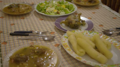 a table set with plates of vori vori, traditional paraguayan soup made with meat, a basket of cooked cassava, cabbage salad in the background, and a stuffed chicken