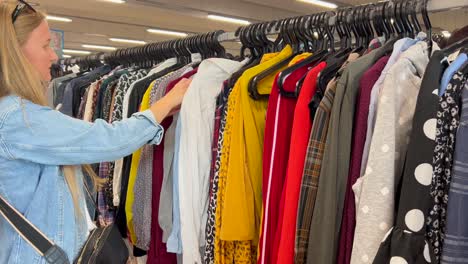young woman selecting fuchsia sweater in dressing room, carefully examining sleeve length, checking appearance in mirror while making expressive gestures. concept of buying women clothes