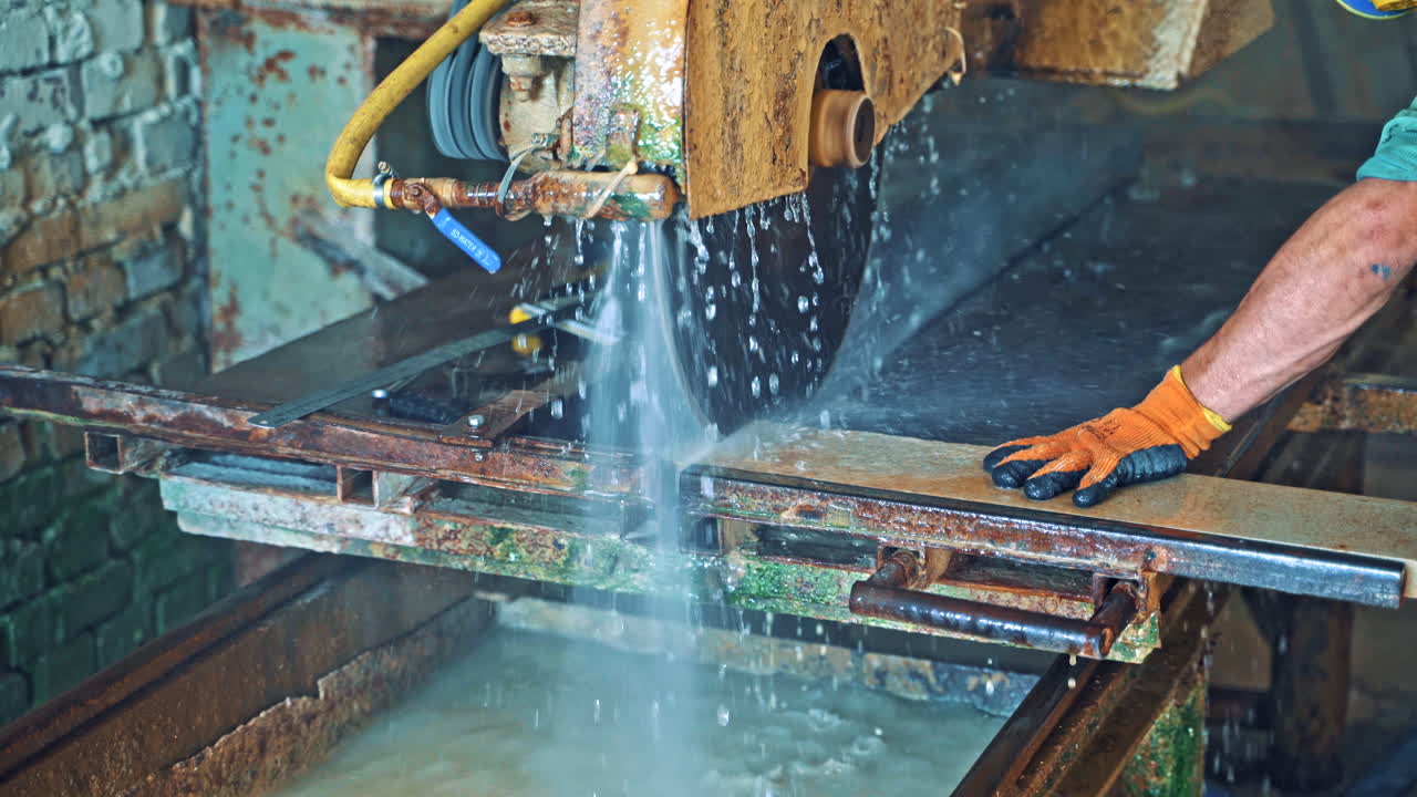 Automated circular saw cuts the stone slab at industrial factory. Process of cutting stone stove with water. Worker controls the electric cutter machine.