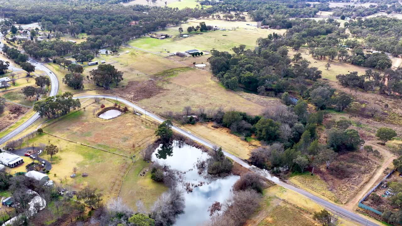 Aerial footage captures a sweeping view of rural Coonabarabran, New South Wales, with open fields, ponds, scattered homes, and winding roads under soft daylight