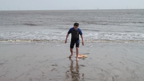 young boy in a wetsuit on a beach digging in the sand