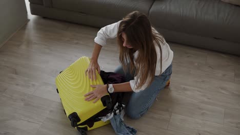 preparando la bolsa para el viaje. mujer joven empacando y tratando desesperadamente de cerrar la maleta llena y cierra una cremallera en ella mientras