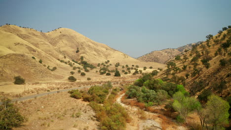 flying through a valley between mountains in the high desert landscape of southern california while a vehicle drives along a road - aerial view