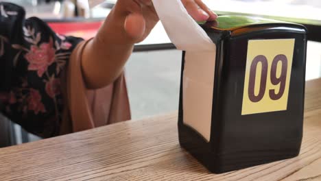 mujer tomando servilleta del dispensador en una mesa del restaurante número 09