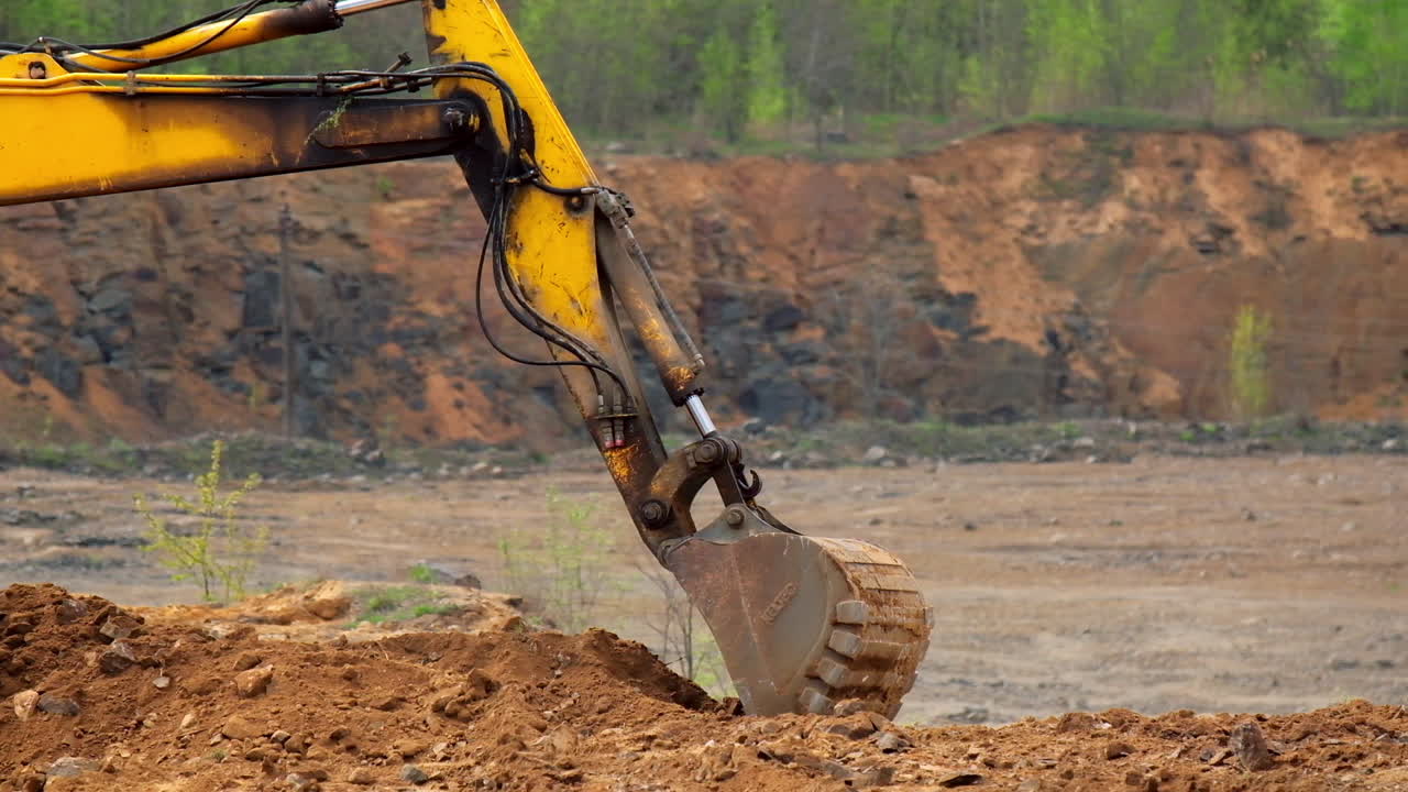 Big excavator bucket scoops up the ground. Yellow metal excavator machine with big shovel digs up the soil. Slow motion.