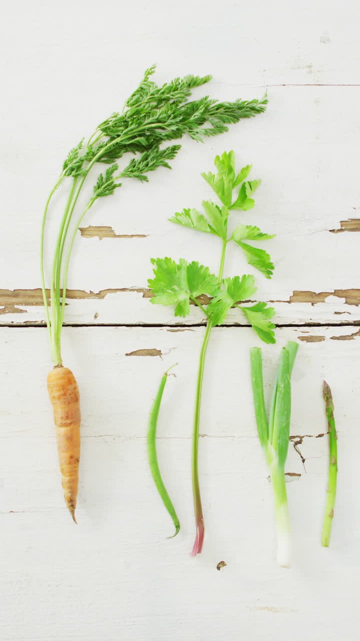vídeo vertical de zanahorias frescas, frijoles, perejil, apio y espárragos sobre un fondo rústico blanco