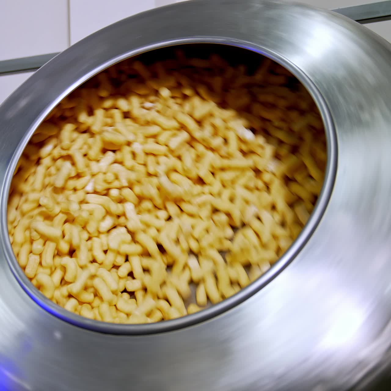 Round metal tank with corn sticks being rotated at the factory automated production. Sweet crispy snacks manufacturing