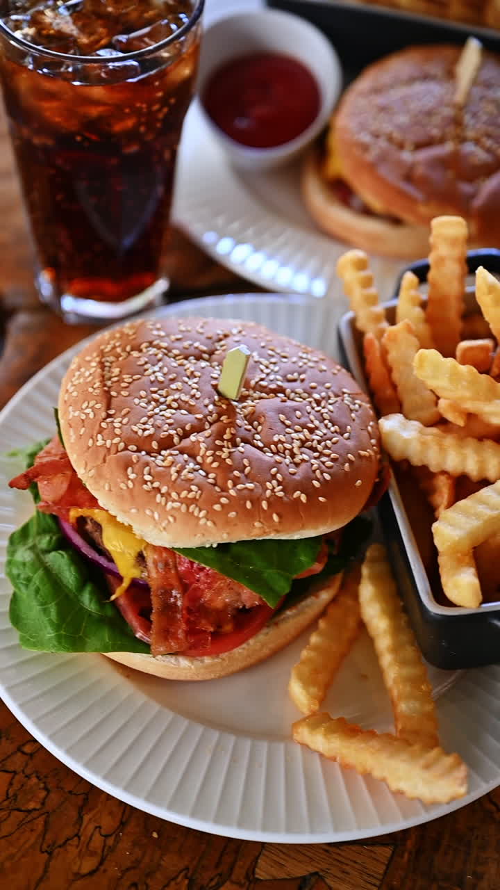 Burger with french fries and ketchup served on plate. Cheeseburger with bacon, fries, and ketchup in cafe setting with warm light