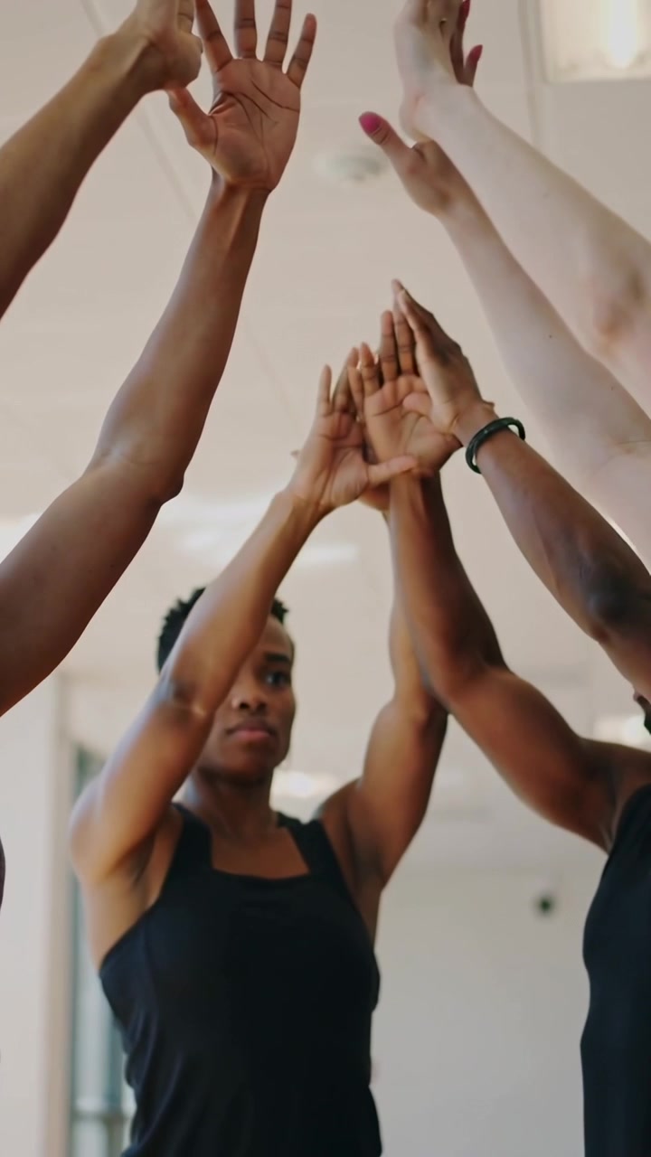 Vertical video: Framing woman in tank top leading team stacking raising hands for warmup in studio